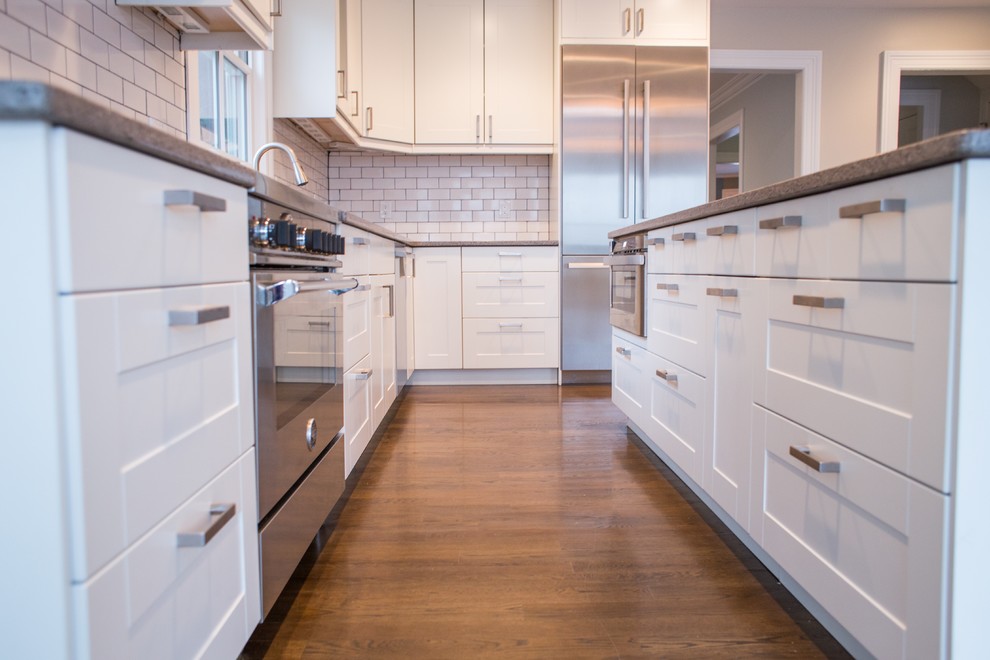 Example of a mid-sized transitional l-shaped dark wood floor open concept kitchen design in New York with an undermount sink, shaker cabinets, white cabinets, granite countertops, white backsplash, subway tile backsplash, stainless steel appliances and an island