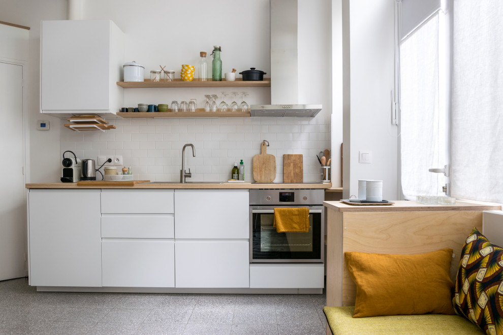 Design ideas for a small contemporary single-wall open plan kitchen in Paris with a drop-in sink, flat-panel cabinets, white cabinets, wood benchtops, white splashback, subway tile splashback, stainless steel appliances, no island, grey floor and beige benchtop.