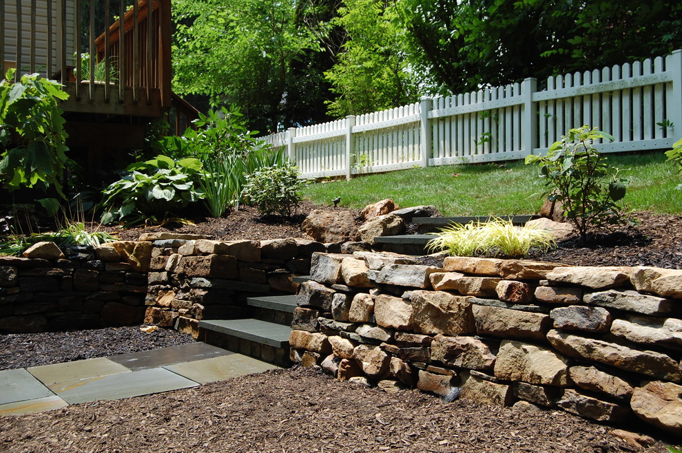 This is an example of a small country backyard partial sun garden in Philadelphia with a retaining wall and natural stone pavers.