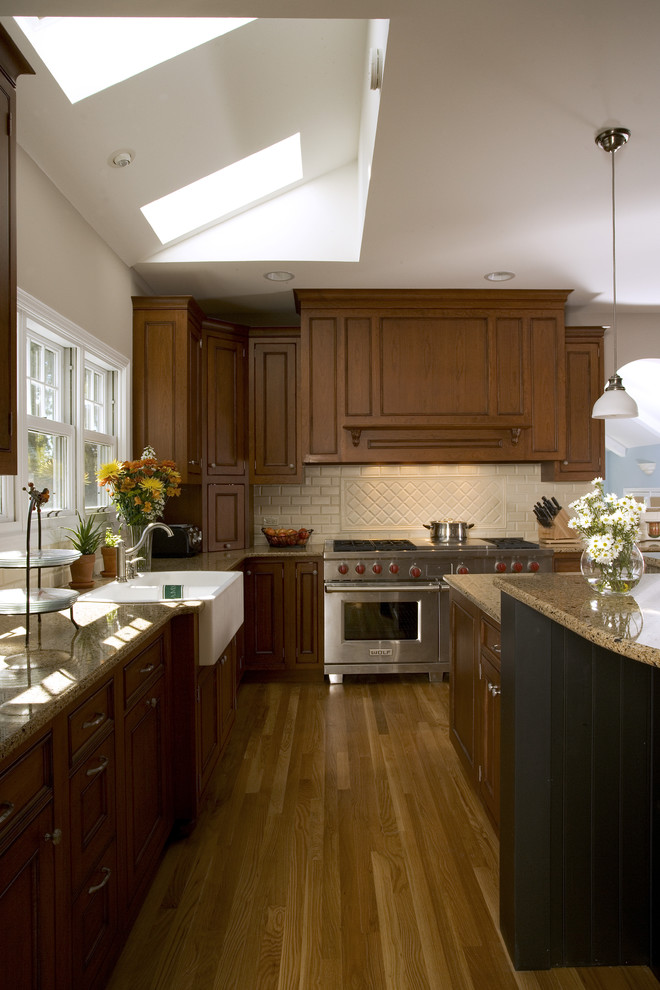 Photo of a traditional u-shaped eat-in kitchen in Chicago with a farmhouse sink, recessed-panel cabinets, medium wood cabinets, granite benchtops, beige splashback, ceramic splashback and panelled appliances.