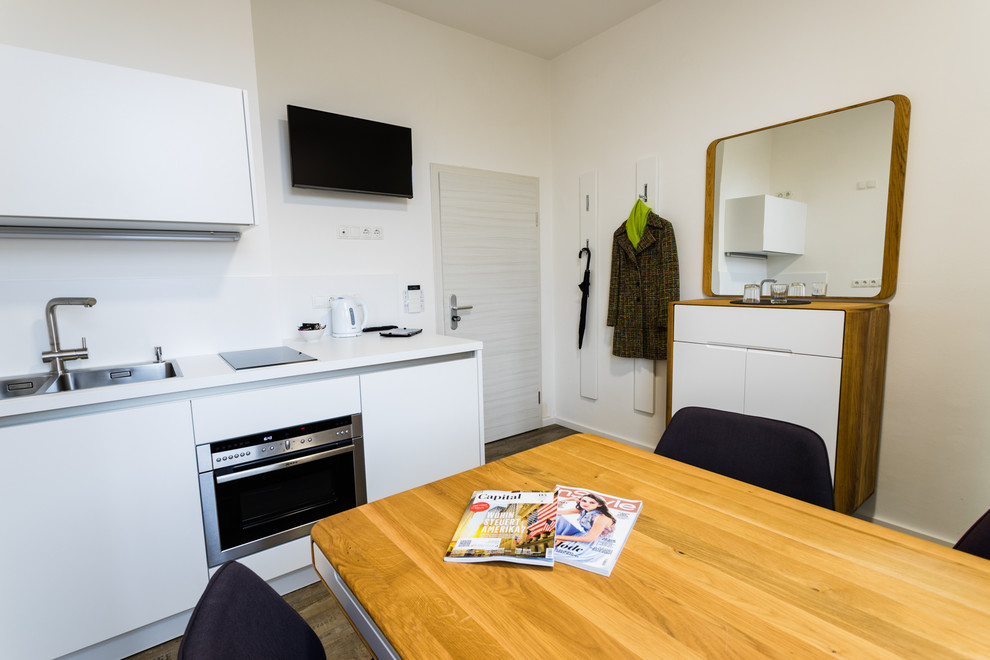 This is an example of a contemporary single-wall eat-in kitchen in Nuremberg with a drop-in sink, flat-panel cabinets, white cabinets, white appliances, medium hardwood floors and no island.