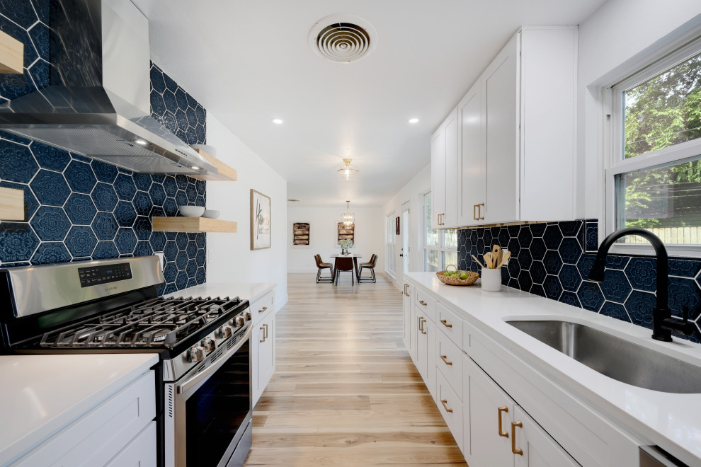 Design ideas for a transitional galley kitchen in Austin with an undermount sink, shaker cabinets, white cabinets, blue splashback, stainless steel appliances, light hardwood floors, no island, beige floor and white benchtop.