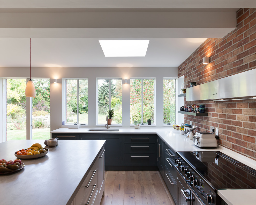 Design ideas for a large contemporary l-shaped eat-in kitchen in London with a drop-in sink, flat-panel cabinets, grey cabinets, concrete benchtops, panelled appliances, medium hardwood floors and a peninsula.
