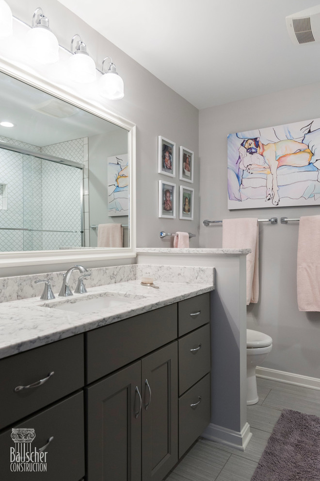 This is an example of a small traditional kids bathroom in Cincinnati with flat-panel cabinets, grey cabinets, an alcove tub, a shower/bathtub combo, a one-piece toilet, white tile, porcelain tile, grey walls, porcelain floors, an undermount sink, granite benchtops, grey floor, a sliding shower screen and grey benchtops.
