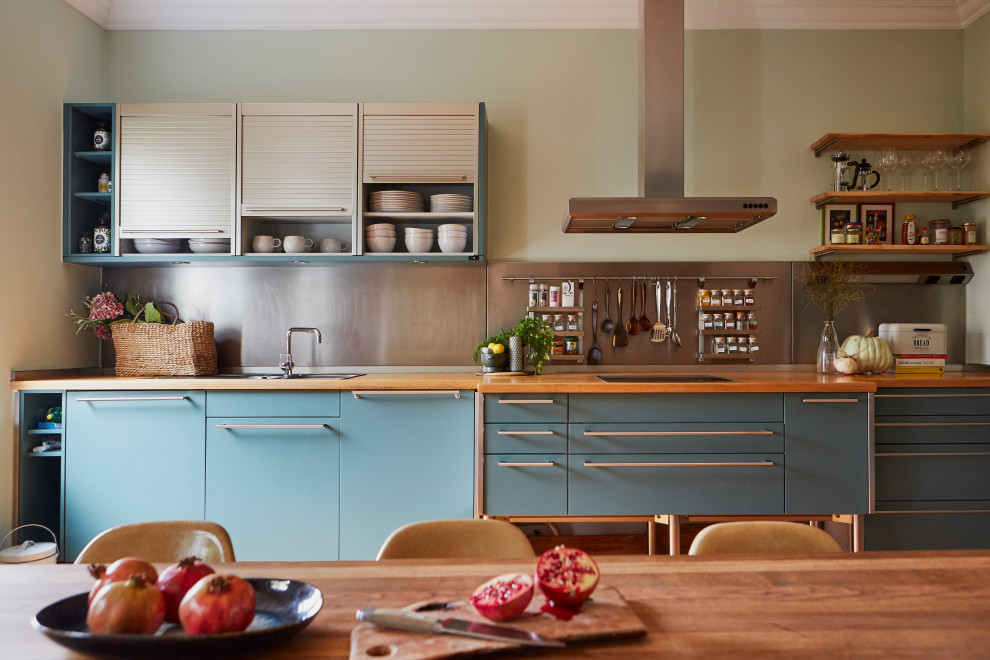 Design ideas for an eclectic single-wall eat-in kitchen in London with a drop-in sink, flat-panel cabinets, blue cabinets, wood benchtops, metallic splashback, no island and brown benchtop.