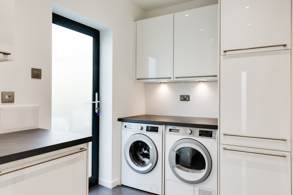 This is an example of a large contemporary galley laundry room in Hampshire with an integrated sink, flat-panel cabinets, grey cabinets, quartzite benchtops, green splashback, glass sheet splashback and porcelain floors.