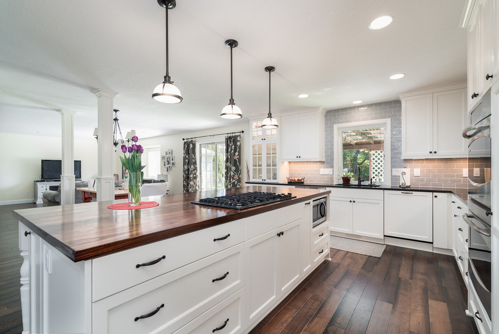 Mid-sized country l-shaped eat-in kitchen in Portland with an integrated sink, flat-panel cabinets, white cabinets, wood benchtops, grey splashback, subway tile splashback, stainless steel appliances, dark hardwood floors and with island.