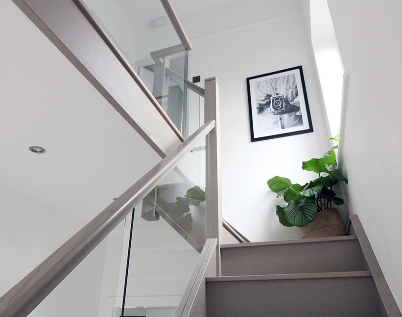 Photo of a mid-sized scandinavian wood l-shaped staircase in West Midlands with wood risers and glass railing.