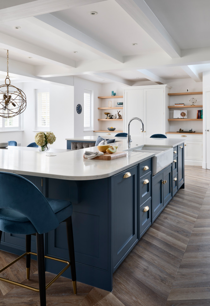Inspiration for a large modern eat-in kitchen in Buckinghamshire with an integrated sink, shaker cabinets, blue cabinets, quartzite benchtops, white splashback, glass sheet splashback, black appliances, light hardwood floors, with island, beige floor, white benchtop and exposed beam.