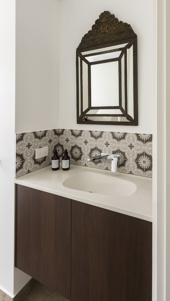 Design ideas for a contemporary powder room in Melbourne with dark wood cabinets, solid surface benchtops, flat-panel cabinets, multi-coloured tile, porcelain tile, white walls, porcelain floors, an integrated sink, brown floor and white benchtops.