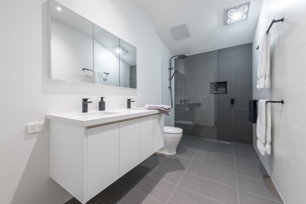 This is an example of a mid-sized modern master bathroom in Other with raised-panel cabinets, white cabinets, an open shower, a one-piece toilet, gray tile, ceramic tile, grey walls, ceramic floors, an integrated sink, engineered quartz benchtops, grey floor, a hinged shower door, white benchtops, a single vanity and a floating vanity.