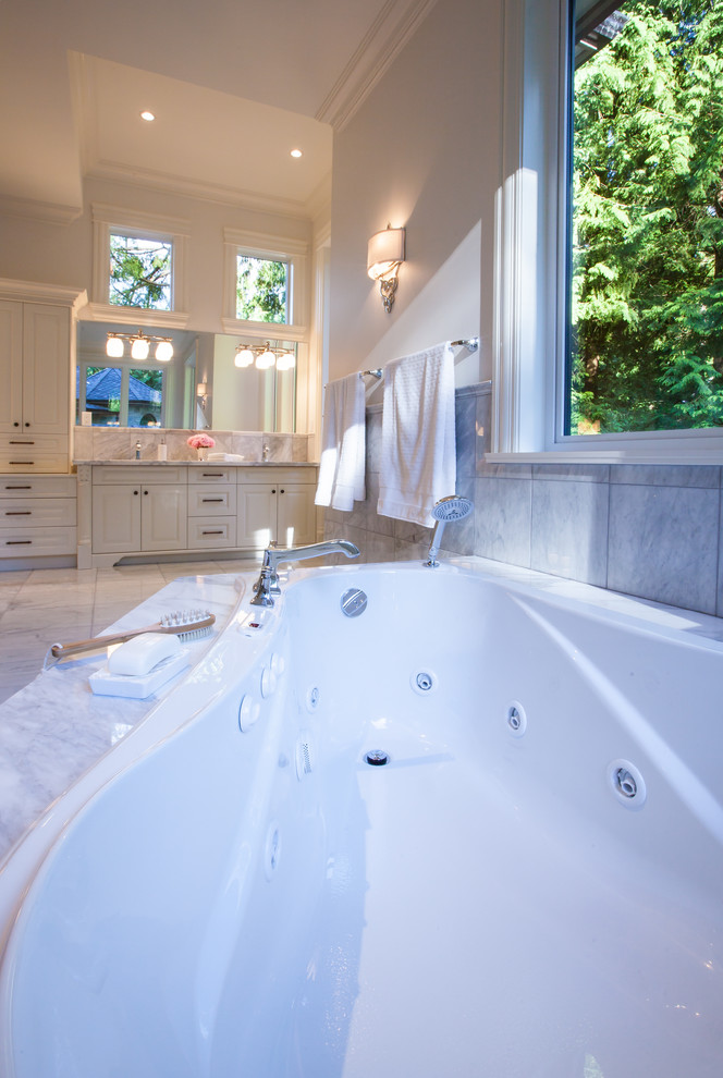 Photo of an expansive transitional master bathroom in Vancouver with an undermount sink, recessed-panel cabinets, white cabinets, marble benchtops, a drop-in tub, a corner shower, a one-piece toilet, gray tile, stone slab, white walls and marble floors.
