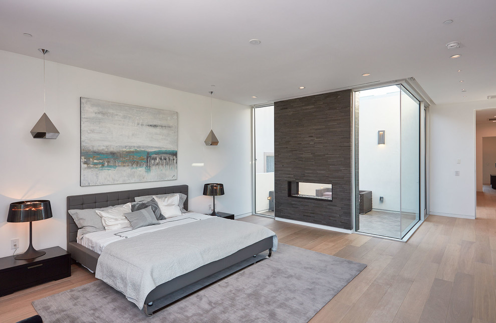This is an example of a contemporary master bedroom in Los Angeles with white walls, light hardwood floors and a two-sided fireplace.