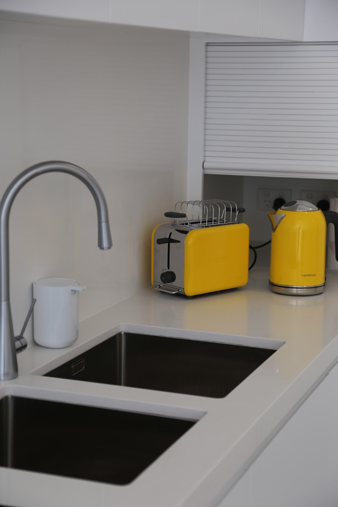 Photo of a small modern l-shaped eat-in kitchen in Sydney with no island, flat-panel cabinets, white cabinets, solid surface benchtops, white splashback, stone slab splashback, coloured appliances, an undermount sink and porcelain floors.