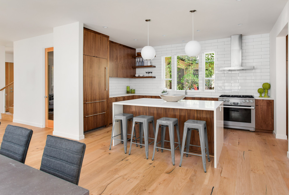 Design ideas for a midcentury l-shaped kitchen in Los Angeles with an undermount sink, flat-panel cabinets, dark wood cabinets, white splashback, stainless steel appliances, light hardwood floors, with island, beige floor and white benchtop.