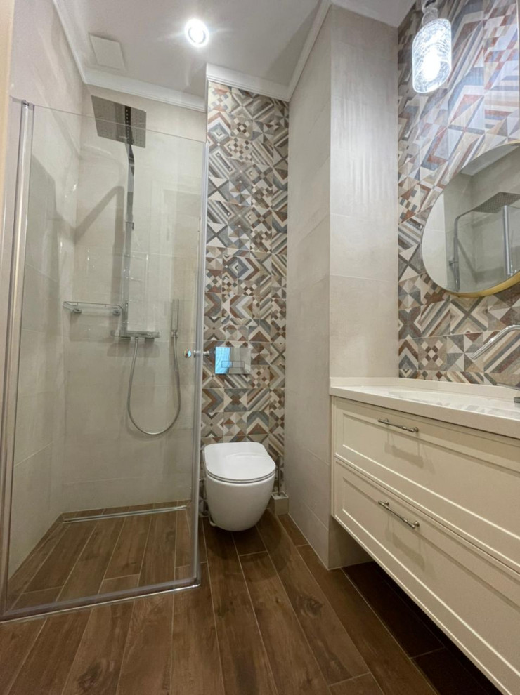 Bild på ett litet skandinaviskt beige beige badrum med dusch, med luckor med upphöjd panel, beige skåp, en kantlös dusch, en vägghängd toalettstol, beige kakel, keramikplattor, beige väggar, klinkergolv i keramik, ett integrerad handfat, bänkskiva i akrylsten, brunt golv och dusch med gångjärnsdörr