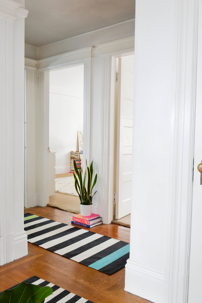 This is an example of a small eclectic hallway in San Francisco with white walls and medium hardwood floors.