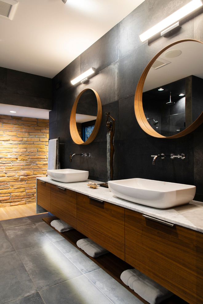 Inspiration for a large contemporary bathroom in Omaha with flat-panel cabinets, dark wood cabinets, a freestanding tub, an open shower, a one-piece toilet, black tile, porcelain tile, black walls, porcelain floors, a vessel sink, marble benchtops, grey floor, a hinged shower door and white benchtops.