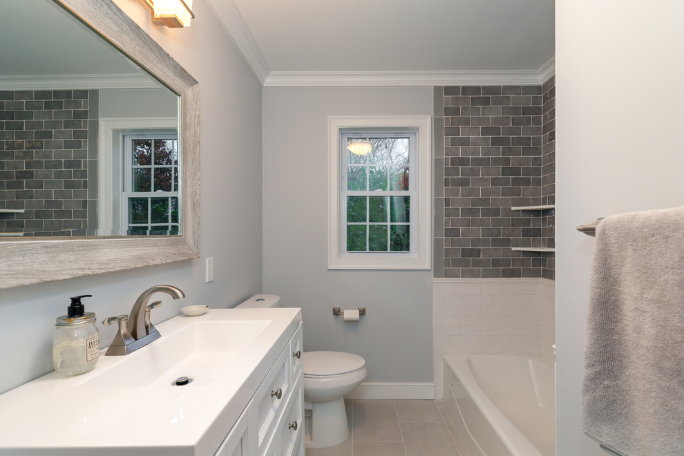 This is an example of a mid-sized traditional 3/4 bathroom in New York with a corner shower, a two-piece toilet, white tile, ceramic tile, grey walls, porcelain floors, an integrated sink, solid surface benchtops, grey floor, a hinged shower door, white benchtops and an alcove tub.