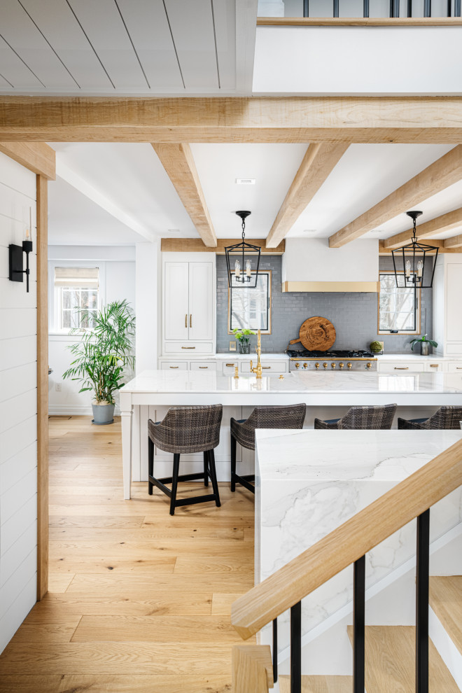 Inspiration for a mid-sized country eat-in kitchen in Philadelphia with an undermount sink, shaker cabinets, marble benchtops, grey splashback, subway tile splashback, stainless steel appliances, light hardwood floors, with island, brown floor, white benchtop and exposed beam.