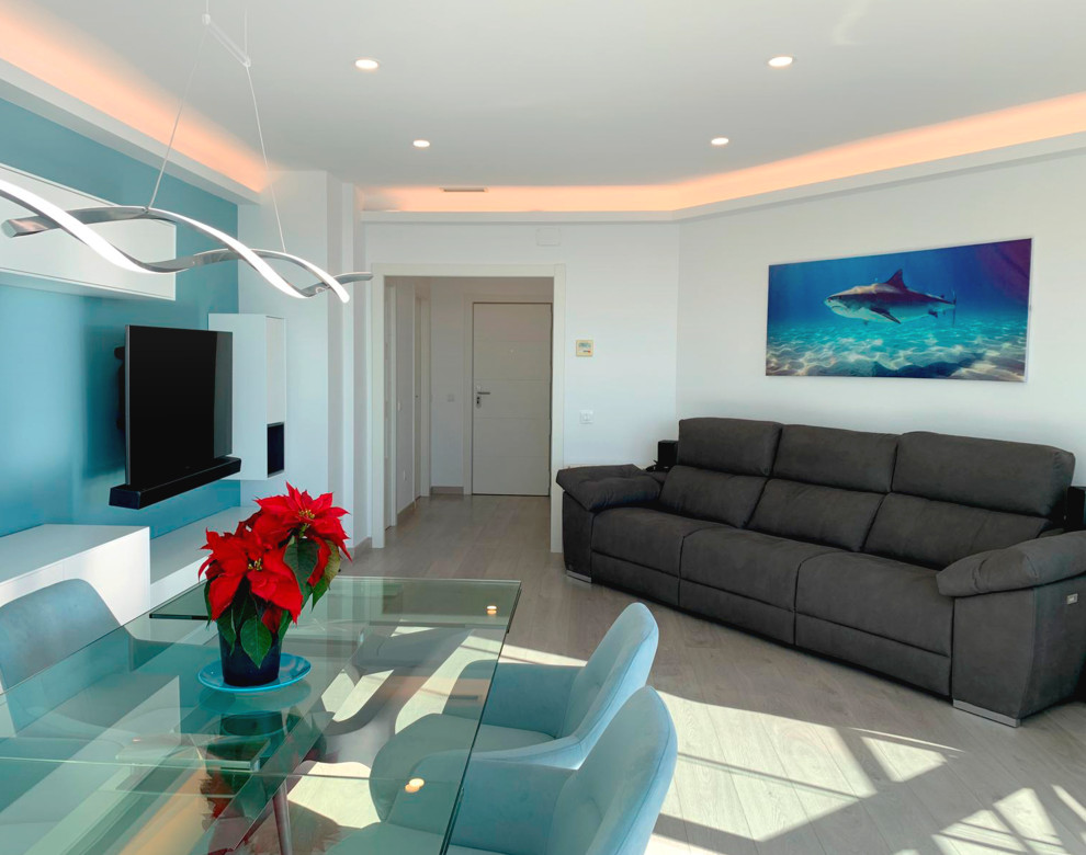 Diseño de salón abierto y blanco costero de tamaño medio con paredes blancas, televisor colgado en la pared, suelo beige, suelo de madera clara y bandeja