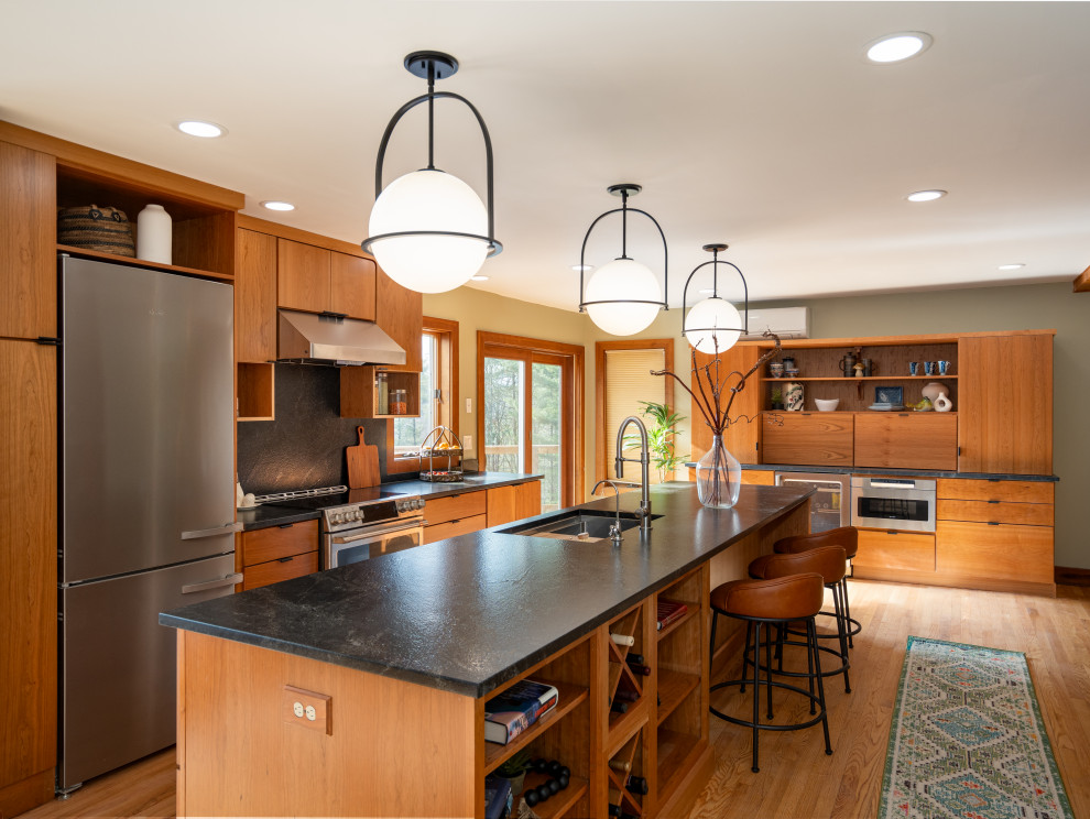 Inspiration for a large contemporary l-shaped medium tone wood floor and brown floor kitchen remodel with a single-bowl sink, flat-panel cabinets, granite countertops, black backsplash, granite backsplash, stainless steel appliances, an island, black countertops and medium tone wood cabinets
