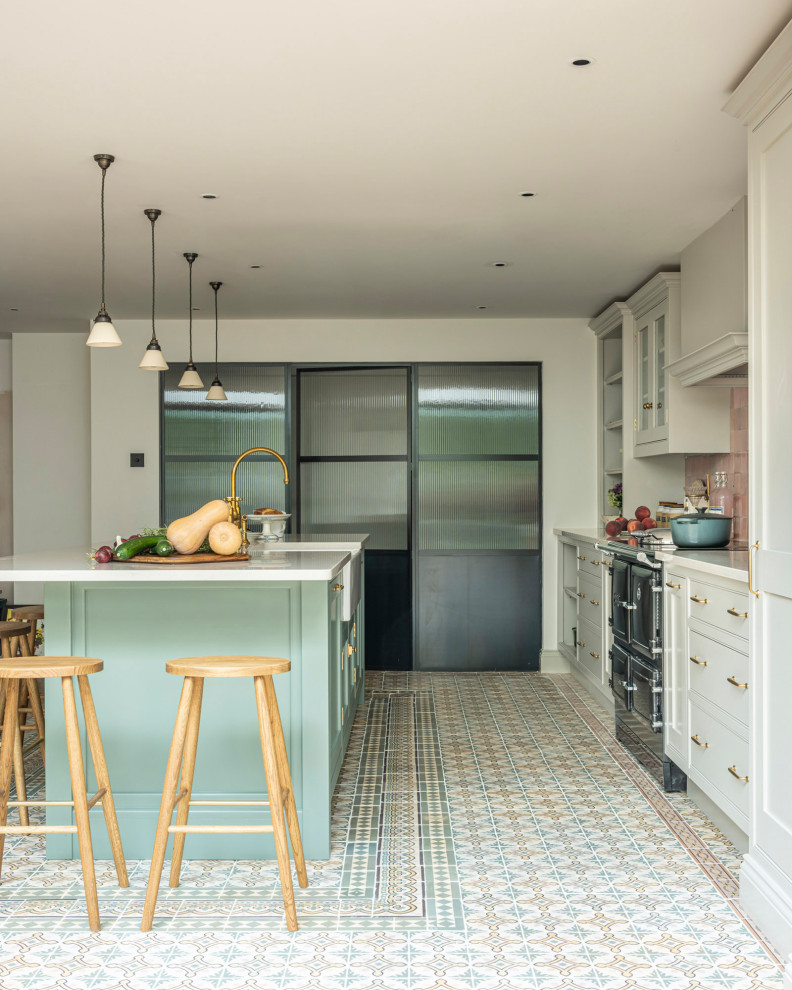 Inspiration for a transitional eat-in kitchen in Buckinghamshire with a farmhouse sink, shaker cabinets, green cabinets, solid surface benchtops, pink splashback, ceramic splashback, black appliances, ceramic floors, with island and white benchtop.