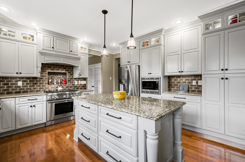 This is an example of a large traditional l-shaped eat-in kitchen in Philadelphia with an undermount sink, raised-panel cabinets, white cabinets, granite benchtops, brown splashback, stainless steel appliances, with island, terra-cotta splashback and medium hardwood floors.