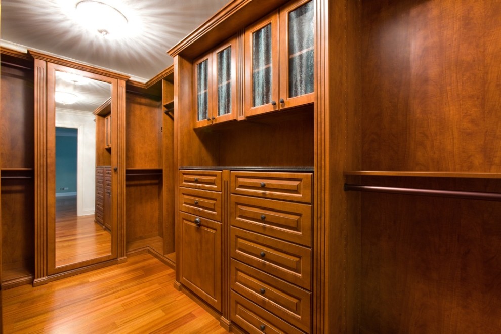 Inspiration for a large traditional gender-neutral walk-in wardrobe in Chicago with raised-panel cabinets, medium hardwood floors and medium wood cabinets.