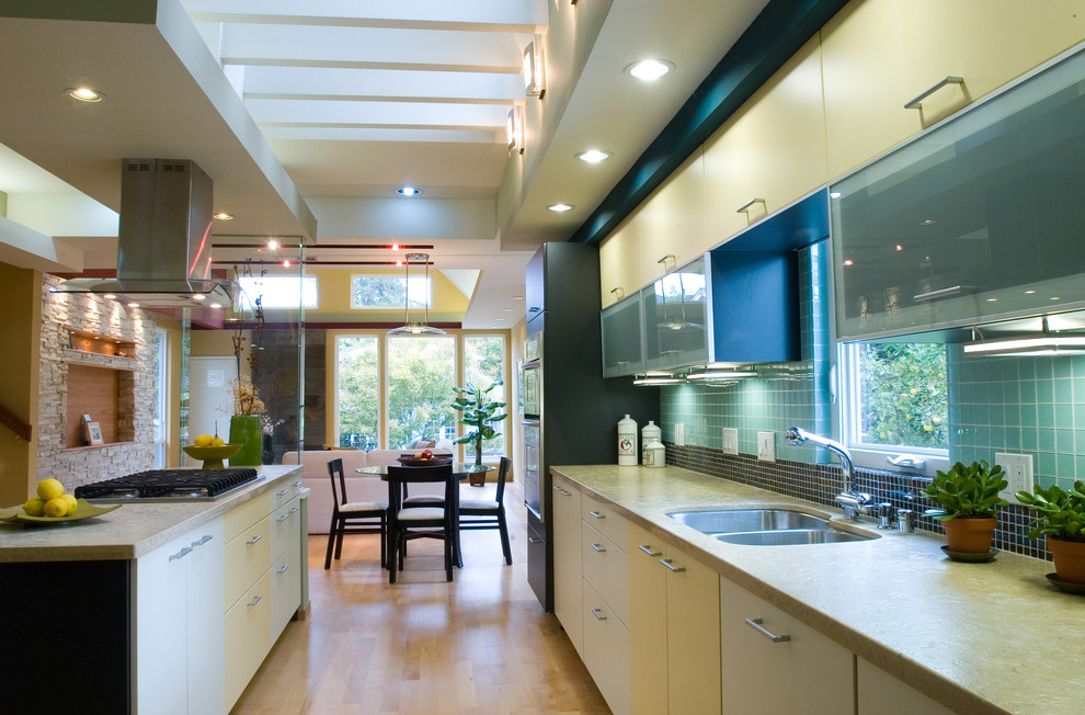 This is an example of a modern kitchen in San Francisco with an undermount sink, flat-panel cabinets, yellow cabinets, limestone benchtops, glass tile splashback, stainless steel appliances, medium hardwood floors and with island.