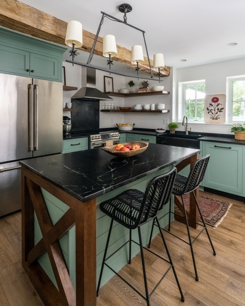 Small country l-shaped separate kitchen in Philadelphia with a farmhouse sink, shaker cabinets, green cabinets, soapstone benchtops, black splashback, stone slab splashback, stainless steel appliances, laminate floors, with island, brown floor and black benchtop.