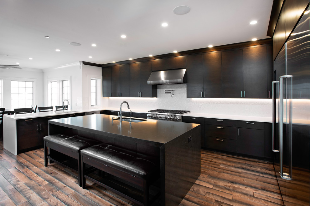 Large modern u-shaped eat-in kitchen in New York with an undermount sink, flat-panel cabinets, dark wood cabinets, solid surface benchtops, white splashback, mosaic tile splashback, stainless steel appliances, dark hardwood floors, with island, brown floor and white benchtop.