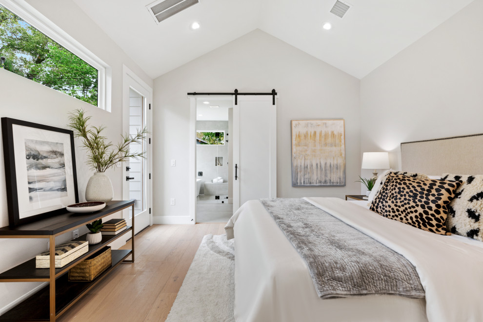 This is an example of a country master bedroom in Austin with white walls, light hardwood floors and vaulted.