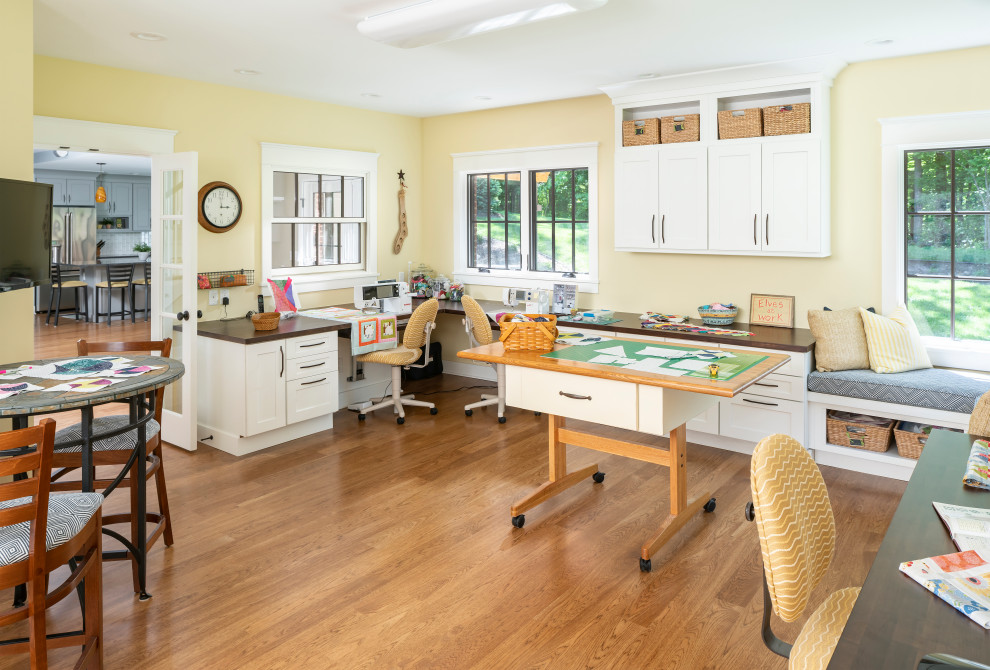 This is an example of a large traditional craft room in Detroit with yellow walls, medium hardwood floors, no fireplace, a built-in desk and beige floor.