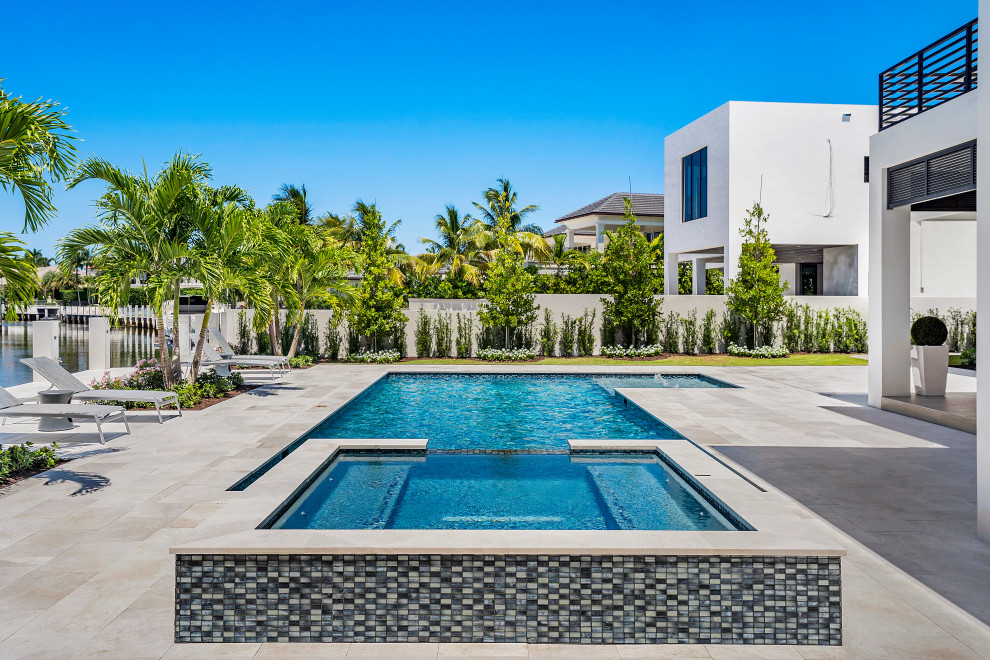 This is an example of a large transitional backyard pool in Miami with natural stone pavers.