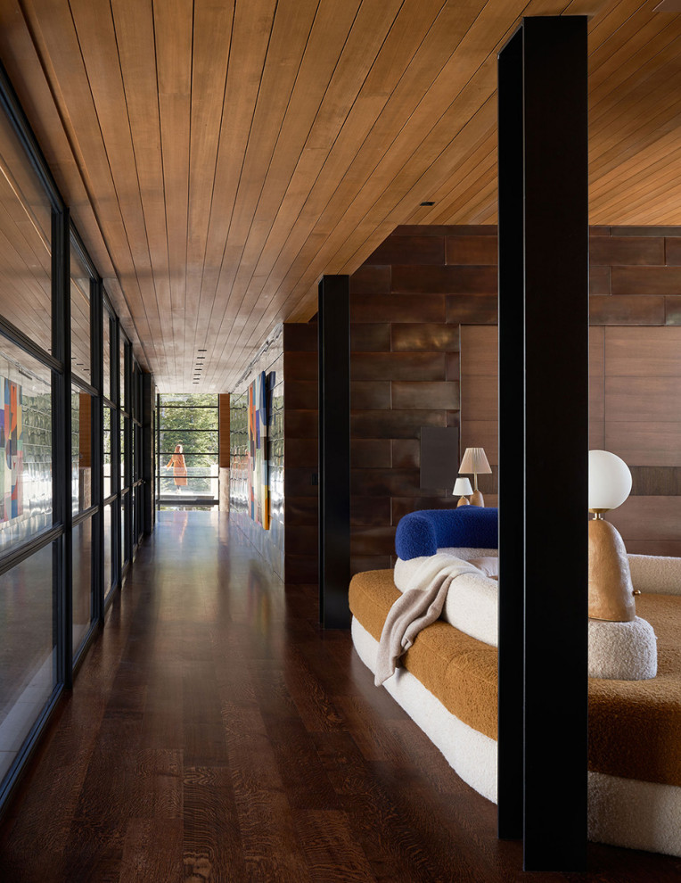На фото: огромный коридор в стиле модернизм с коричневыми стенами, паркетным полом среднего тона, коричневым полом, деревянным потолком и панелями на части стены с