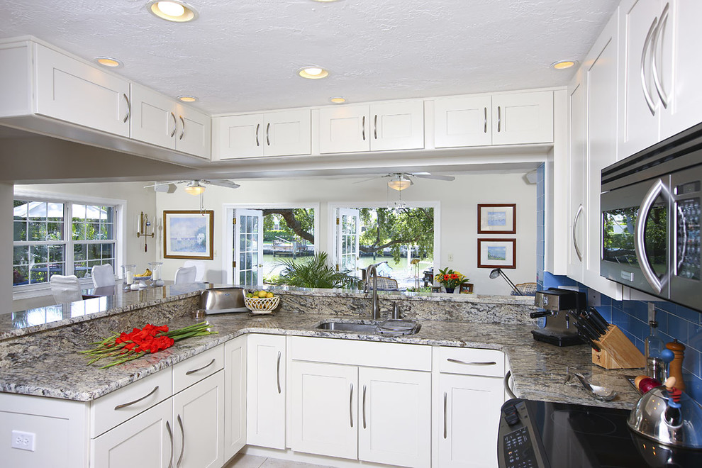 Inspiration for a mid-sized contemporary l-shaped eat-in kitchen in Tampa with a single-bowl sink, flat-panel cabinets, white cabinets, granite benchtops, metallic splashback, metal splashback, stainless steel appliances, limestone floors and beige floor.
