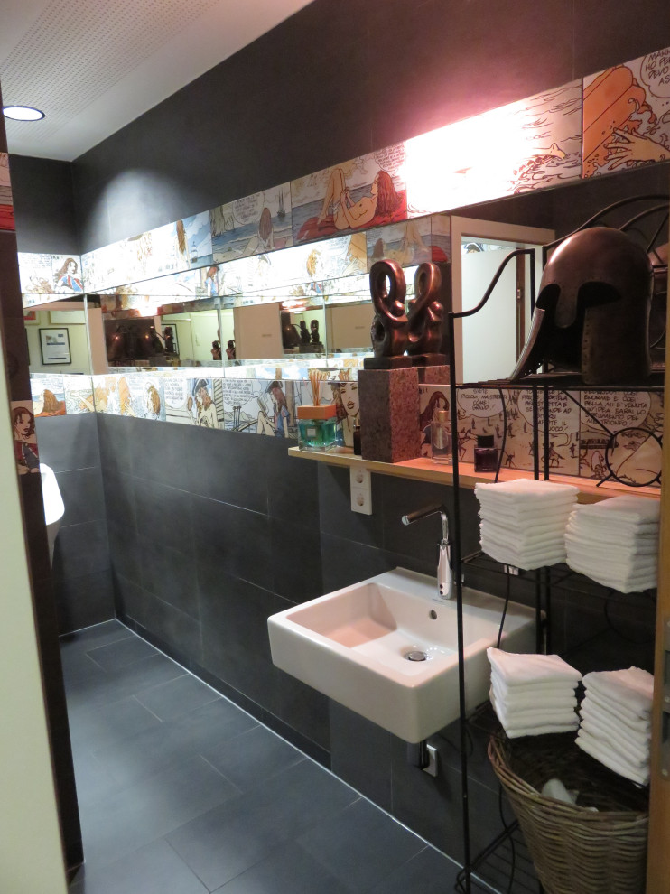 Mid-sized eclectic powder room in Munich with a wall-mount toilet, black tile, ceramic tile, black walls, ceramic floors, a wall-mount sink, glass benchtops, black floor, a floating vanity and recessed.