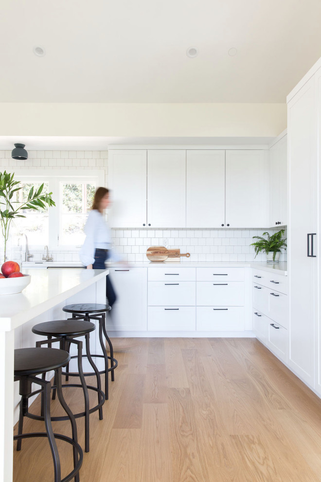 Photo of a large transitional l-shaped kitchen in San Francisco with shaker cabinets, white cabinets, white splashback, subway tile splashback, with island, beige floor and white benchtop.