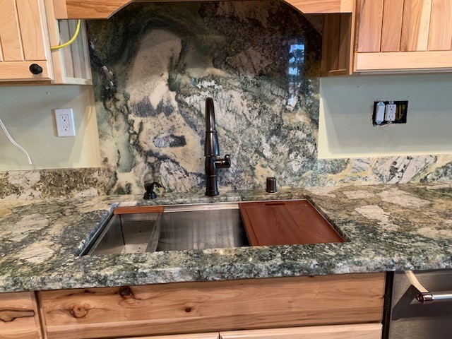 Mid-sized mountain style medium tone wood floor and brown floor open concept kitchen photo with an undermount sink, flat-panel cabinets, light wood cabinets, granite countertops, gray backsplash, stone slab backsplash, stainless steel appliances and gray countertops