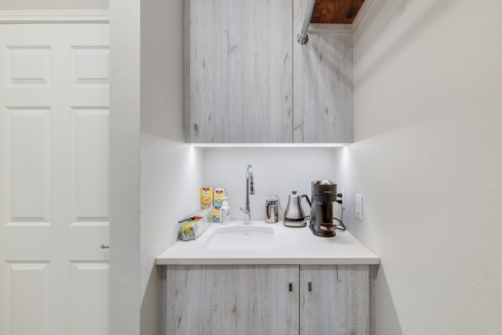 This is an example of a mid-sized transitional galley dedicated laundry room in Austin with an undermount sink, flat-panel cabinets, light wood cabinets, quartz benchtops, grey splashback, timber splashback, grey walls, ceramic floors, a side-by-side washer and dryer, grey floor, grey benchtop and planked wall panelling.