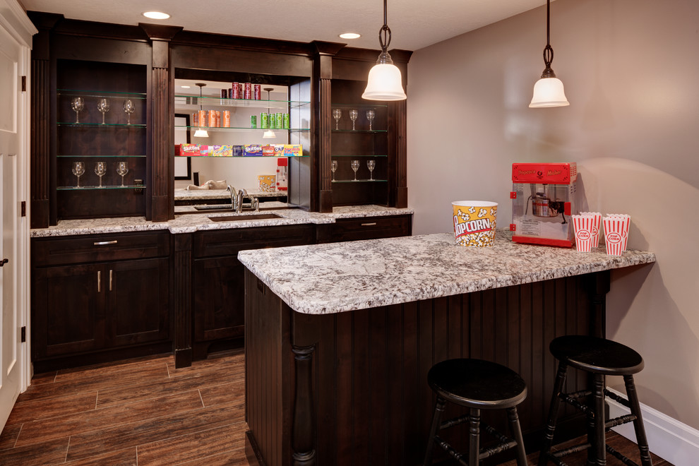 Photo of a mid-sized traditional single-wall seated home bar in Salt Lake City with an undermount sink, shaker cabinets, dark wood cabinets, granite benchtops, dark hardwood floors and brown floor.