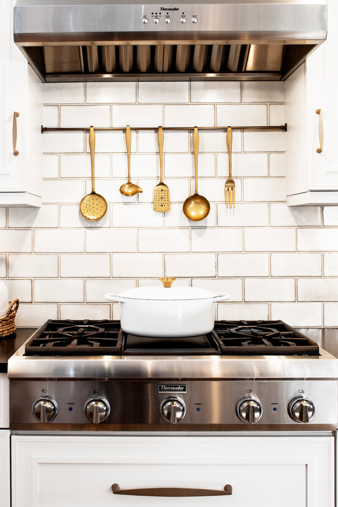 Large transitional u-shaped medium tone wood floor and brown floor eat-in kitchen photo with white backsplash, stainless steel appliances, a farmhouse sink, recessed-panel cabinets, white cabinets, marble countertops, glass tile backsplash and an island