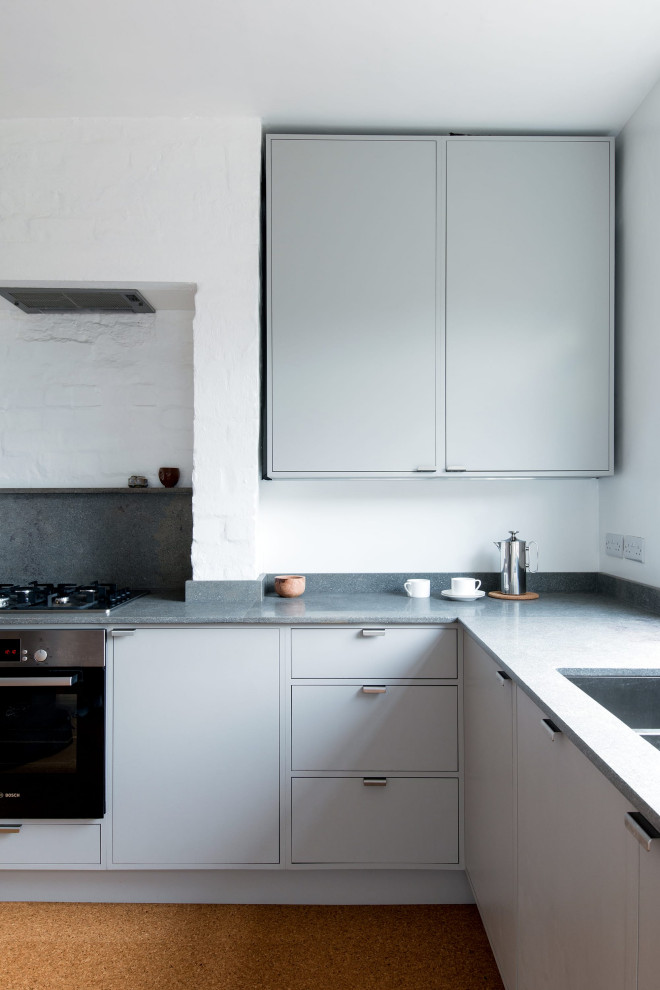 Small contemporary l-shaped eat-in kitchen in London with a double-bowl sink, flat-panel cabinets, grey cabinets, limestone benchtops, grey splashback, limestone splashback, stainless steel appliances, cork floors, no island and grey benchtop.