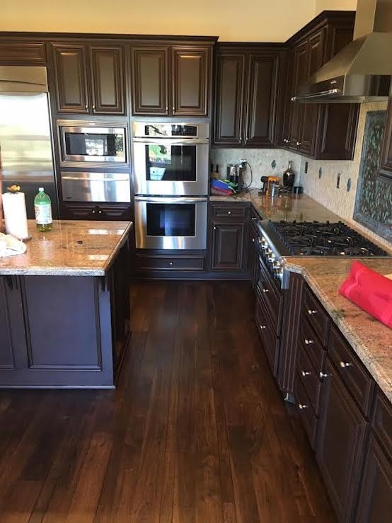 Photo of a mid-sized traditional l-shaped kitchen in Orange County with raised-panel cabinets, brown cabinets, granite benchtops, beige splashback, stone slab splashback, stainless steel appliances, dark hardwood floors, with island and brown floor.