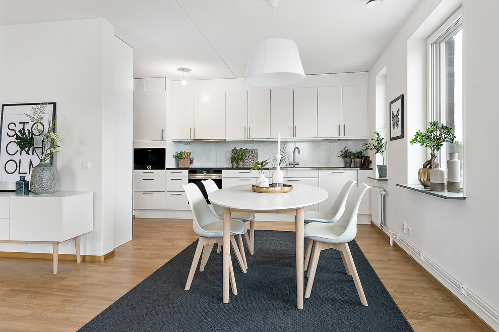 This is an example of a mid-sized scandinavian kitchen/dining combo in Stockholm with white walls, light hardwood floors and no fireplace.