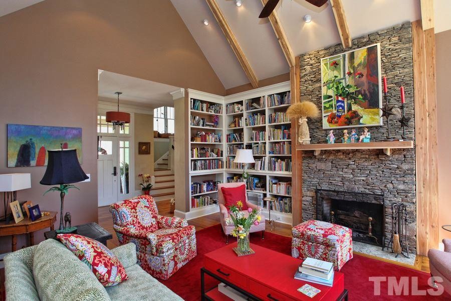 This is an example of an arts and crafts open concept living room in Raleigh with a library, brown walls, medium hardwood floors, a standard fireplace, a stone fireplace surround and no tv.