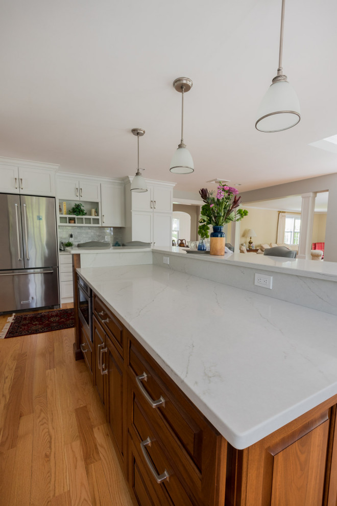 Eat-in kitchen - large transitional l-shaped medium tone wood floor, brown floor and coffered ceiling eat-in kitchen idea in Boston with an undermount sink, shaker cabinets, white cabinets, quartz countertops, gray backsplash, subway tile backsplash, stainless steel appliances, an island and white countertops
