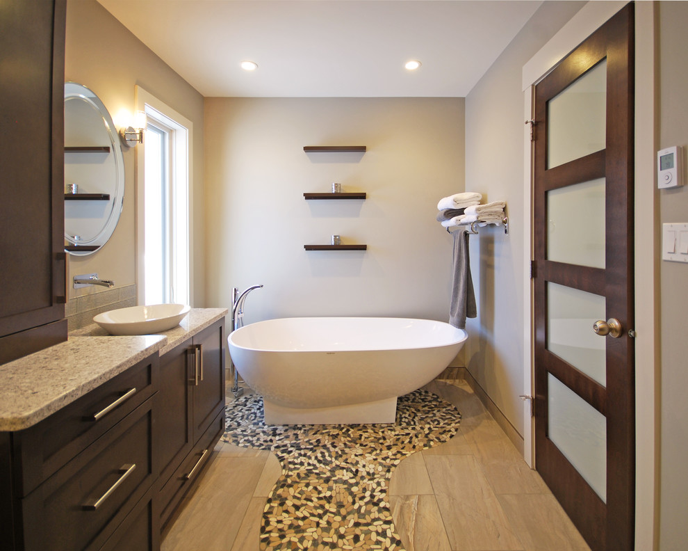 Inspiration for a mid-sized contemporary master bathroom in Edmonton with a vessel sink, flat-panel cabinets, dark wood cabinets, quartzite benchtops, a freestanding tub, brown tile, porcelain tile, grey walls and pebble tile floors.