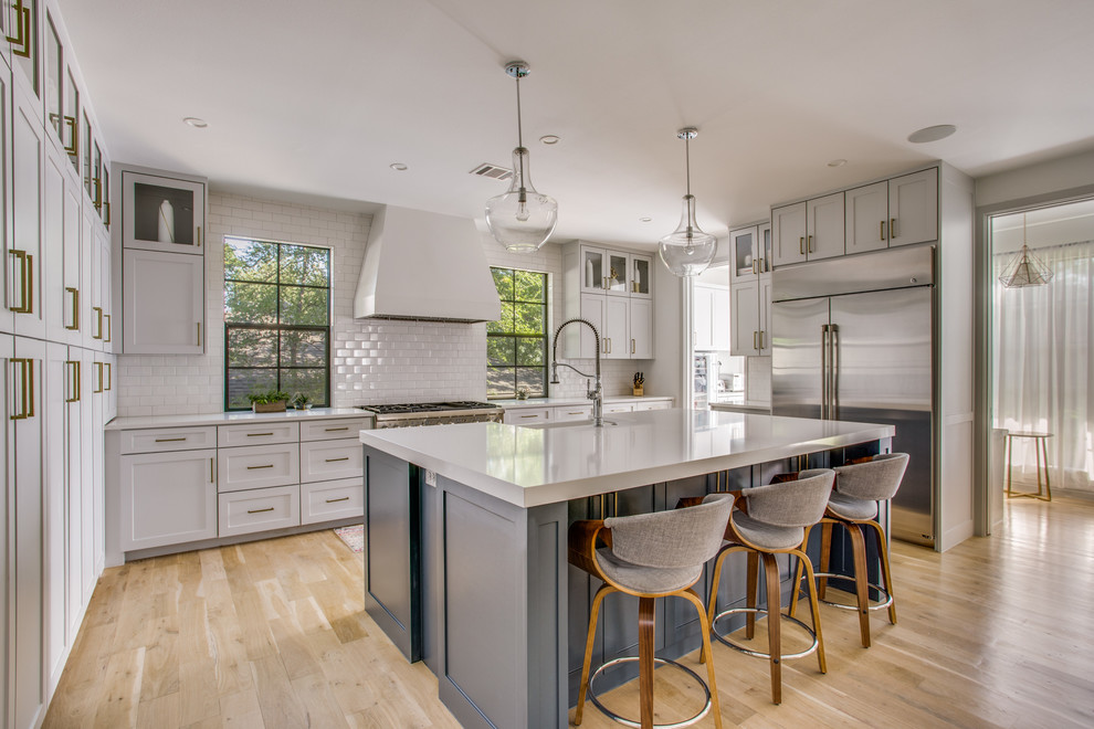 Design ideas for a large transitional u-shaped open plan kitchen in Dallas with a farmhouse sink, shaker cabinets, grey cabinets, quartz benchtops, white splashback, subway tile splashback, stainless steel appliances, light hardwood floors, with island, beige floor and white benchtop.